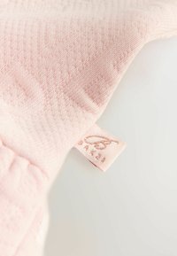 Helles rosa Strickgewebe mit einem strukturierten Muster, ausgestattet mit einem kleinen Etikett, das am Rand "BAKER" in Roségold trägt.