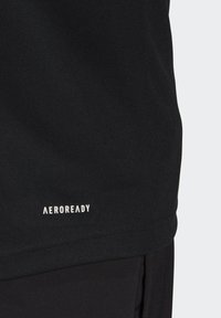 Gros plan sur un short de sport noir et un t-shirt avec un petit logo blanc "AEROREADY" près de l’ourlet du t-shirt.