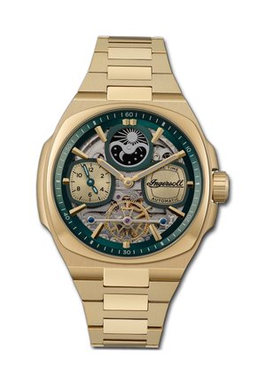 Montre automatique dorée avec une lunette verte, cadran squelette montrant les engrenages, deux sous-cadrans et un bracelet texturé doré.