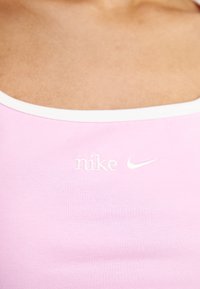 Rosa träningslinne i slät tyg med vit kant och broderad Nike-logotyp på framsidan. Subtil ribbad textur.