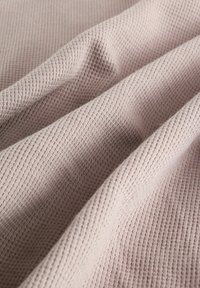 Tkanina v svetloružovej farbe, s textúrovaným povrchom a jemným ryhovaním, prehodená v mäkkých záhyboch, aby ukázala svoju flexibilnú štruktúru.
