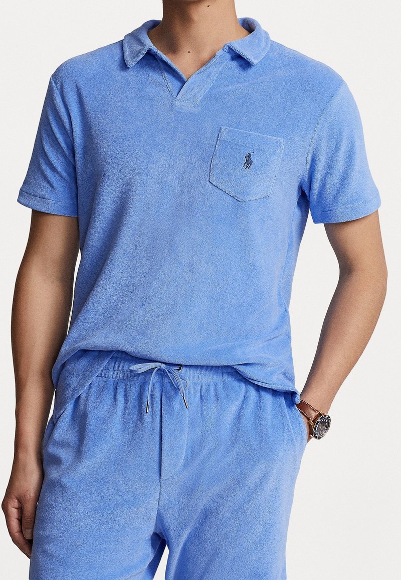 Ljusblå handdukspiké med korta ärmar, treknapps knäppning, bröstficka och broderad logodetalj. Mjuk textur och avslappnad passform.