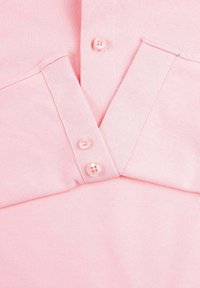 Lichtroze polo met een gestructureerde stof, drie knopen op de sluiting en een kraag met een driehoekige uitsnijding bij de halslijn.
