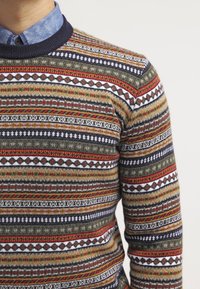 Pull en tricot présentant des rayures multicolores en rouge, marine, crème et vert. Encolure côtelée avec une finition texturée.