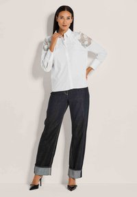 Witte ingezette blouse met kantaccenten op de mouwen, gecombineerd met donkerdenim broeken met omgeslagen manchetten en een paar hakken.