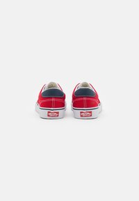 Scarpe da skate in tela rossa con un accento blu navy sul tallone. Suola in gomma bianca e cuciture, con un logo classico sul tallone.