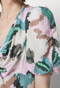Mujer con un vestido de color pastel con mangas abullonadas que presenta un patrón abstracto pixelado en verde, rosa, marrón y negro.