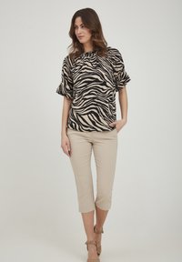 Blusa a righe zebra nera e beige con maniche arricciate, abbinata a pantaloni beige a metà polpaccio e tacchi nudo. Tessuto semplice e morbido, vestibilità casual.
