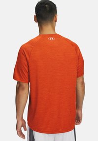 Camiseta atlética roja de mangas cortas con una superficie texturizada. Presenta un cuello redondo y un pequeño logo en la parte posterior cerca del cuello.