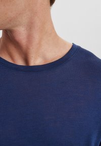 T-shirt in cotone blu navy con collo rotondo, texture liscia e dettagli di cucitura minimi sul colletto. Dettaglio ravvicinato del collo e della spalla.