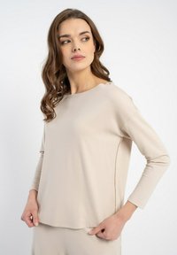Beżowa bluzka z długim rękawem i okrągłym dekoltem, gładka w dotyku, z subtelnymi detalami szwów bocznych. Miękki i dopasowany fason.