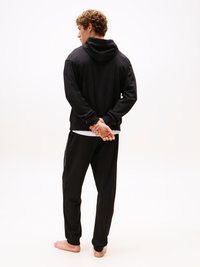 Felpa nera con una vestibilità morbida e cappuccio con cordino, abbinata a pantaloni della tuta neri coordinati con polsini elastici e tasche.