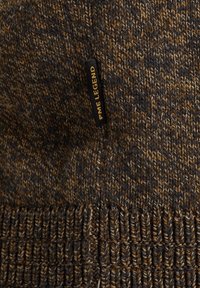 Gros plan sur un tissu tricoté brun et gris foncé avec un bord côtelé et une petite étiquette noire portant l'inscription "PME LEGEND" en lettres jaunes.