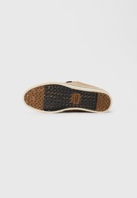 Sola de sapatilha bege com padrão de trilha triangular em preto e castanho e logótipo "etnies" no centro sobre fundo branco liso.