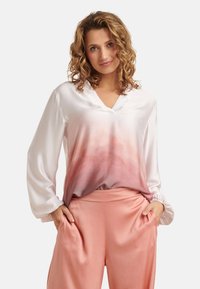 Seidenbluse mit einem sanften Farbverlauf von Weiß zu Hellrosa, mit V-Ausschnitt, langen Ärmeln und elastischen Bündchen; kombiniert mit pfirsichfarbenen , weit geschnittenen Hosen.