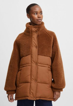 Bruine pufferjack met een gestructureerde, pluizige bovenkant en gladde onderste delen. Voorzien van een hoge kraag en oversized, zachte mouwen.