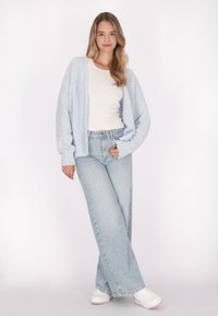Cárdigan azul claro y esponjoso sobre una blusa blanca ajustada, combinado con jeans de pierna ancha de tiro alto de lavado claro y zapatillas blancas.