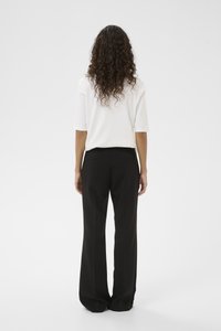 Weißes Kurzarmoberteil kombiniert mit schwarzen, weit geschnittenen Hosen. Glatter Stoff mit lockerem Schnitt; die Hosen verfügen über zwei Gesäßtaschen.