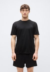 Svart atletisk t-shirt med korta ärmar, rund halsringning, slät textur och diskret logotyp på bröstet, tillsammans med matchande svarta shorts.