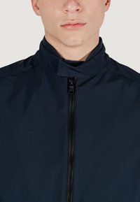 Giacca navale realizzata in tessuto liscio, con colletto alto e zip nera centrale. Design minimalista senza motivi o decorazioni visibili.