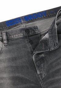 Grå denimbukser med en blå "HUGO | BRODY" label på taljen, der har to sorte knapper og et diskret tekstureret stof.
