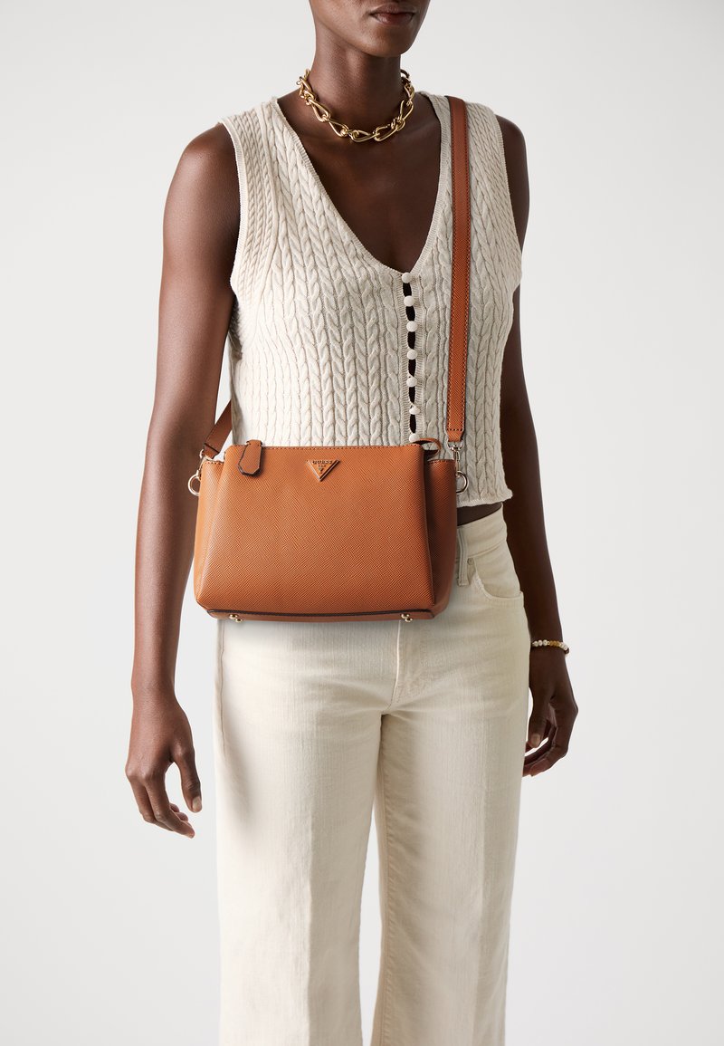 Sac en cuir texturé marron en bandoulière avec un logo triangulaire, complété par une longue sangle et des détails en matériel doré.