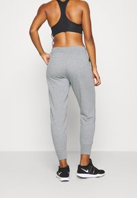 Graue, schmal zulaufende Jogginghosen aus weichem Material mit elastischen Bündchen, kombiniert mit schwarzen Sportschuhen. Sie besitzen ein schlichtes Design und eine entspannte Passform.