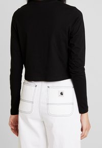 Svart långärmad cropped topp som är kombinerad med vita högmidjade byxor med en lappetikett och synlig sömnad på fickorna.