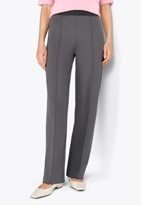 Pantaloni grigi a vita alta con una texture liscia, dotati di una cinturini elastico nero e dettagli con cucitura frontale. Abbinati a scarpe bianche.