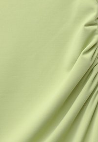 Lichtgroene textuurstof met een fijne ribstructuur, die zachtjes valt met lichte plooien en zijn gladde oppervlak en elasticiteit toont.
