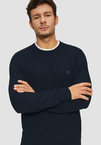 Marineblauer Strickpullover mit strukturiertem Design, Rundhalsausschnitt und gerippten Bündchen, mit einem kleinen schwarzen Logoakzent auf der Brust.