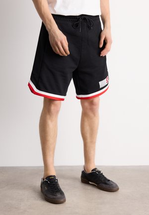 Black sports shorts with red and white trim, featuring an elastic waistband with drawstring and a visible brand logo patch on the side.