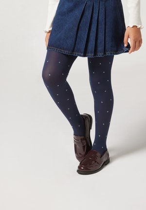 Marineblaue Strumpfhosen mit kleinen weißen Herzmustern, kombiniert mit einem denim Faltenrock und glänzenden burgunderfarbenen Loafers.