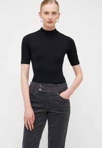 Svart kortermet turtleneck topp kombinert med grå kordfløyel bukser med to frontlommer og knappdekorasjoner. Jevn tekstur overalt.
