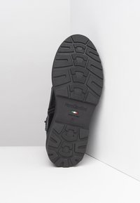 Schwarzer Stiefel mit strukturiertem Gummi-Ausgang, der ein geripptes Muster und ein eingraviertes Markenlogo aufweist. Hergestellt in Italien, Größe 37.