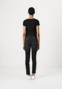 Black ribbed crop top and black skinny jeans with a frayed hem. Model wears white sneakers. Image shows a rear view against a plain background.