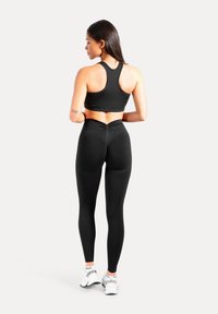 Schwarzer Sport-BH und Leggings aus dehnbarem Stoff, mit Racerback-Design und hohem Bund, kombiniert mit weißen Sportschuhen.