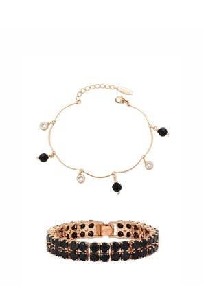 Armbanden met goudkleurige tint en zwarte en heldere edelsteentjes; de ene is een fijn kettinkje met hangende bedeltjes, de andere een brede band met twee rijen stenen.