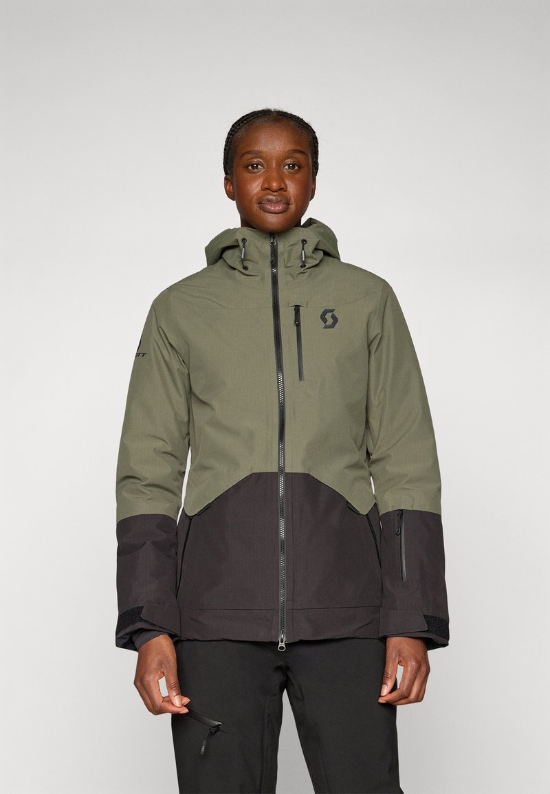 Wasserdichte Jacke mit der oberen Hälfte in Grün und der unteren Hälfte in Schwarz. Mit Kapuze, Reißverschlusstaschen und verstellbaren Bündchen.