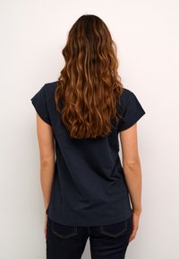 Tumed sinine lühikeste varrukatega T-särk, millel on mugav lõige. Pehme puuvillane kangas ja kaardus hem, koos tumedate teksadega.