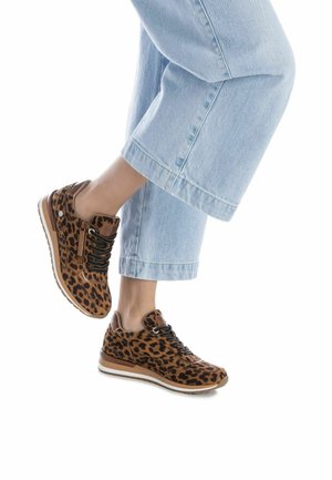 Zapatillas con estampado de leopardo en material de ante marrón, cordones negros y suelas de goma. Combinadas con pantalones de mezclilla recortados en azul claro.