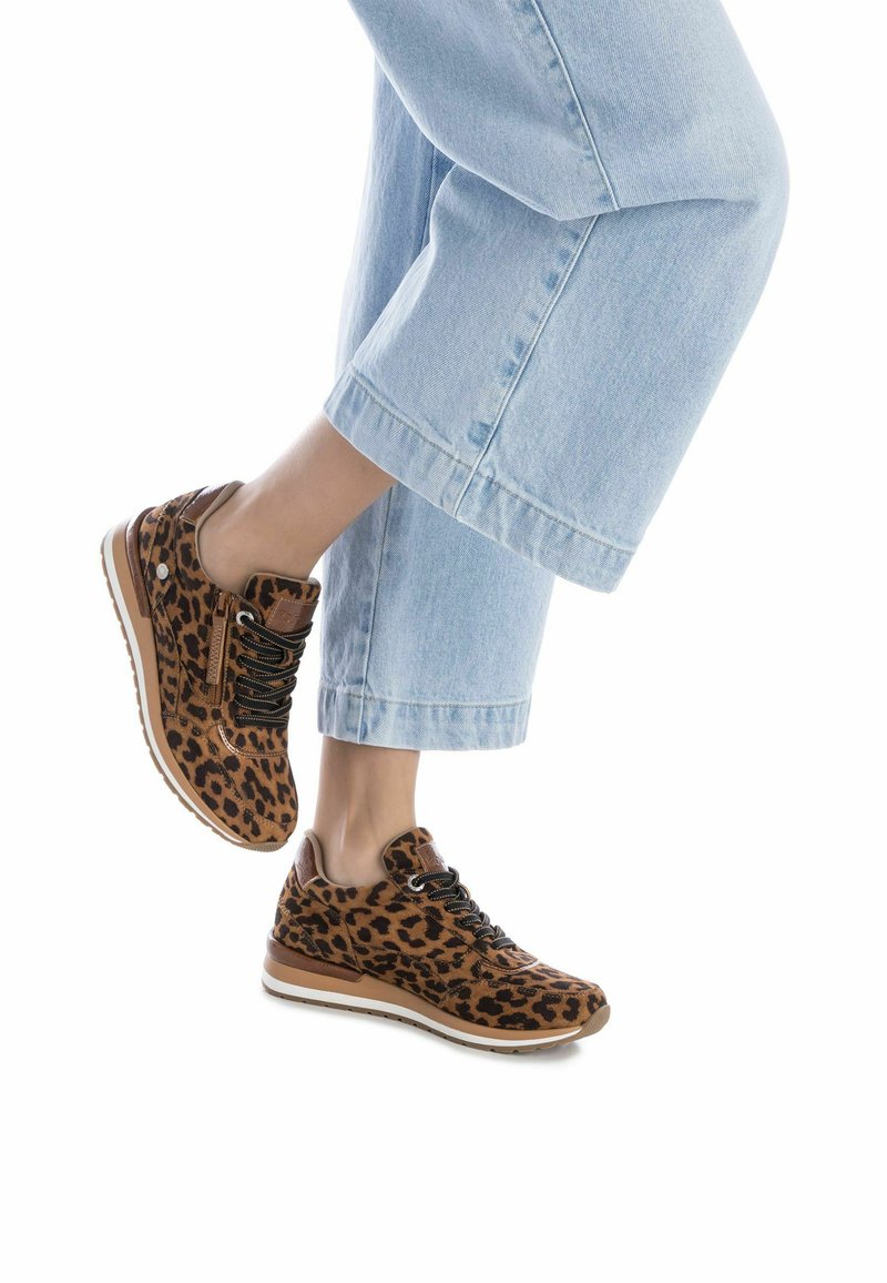 Zapatillas con estampado de leopardo en material de ante marrón, cordones negros y suelas de goma. Combinadas con pantalones de mezclilla recortados en azul claro.