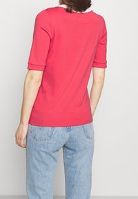 T-shirt rossa a maniche corte con scollo rotondo, texture liscia e silhouette aderente, abbinata a jeans azzurri a vita alta.