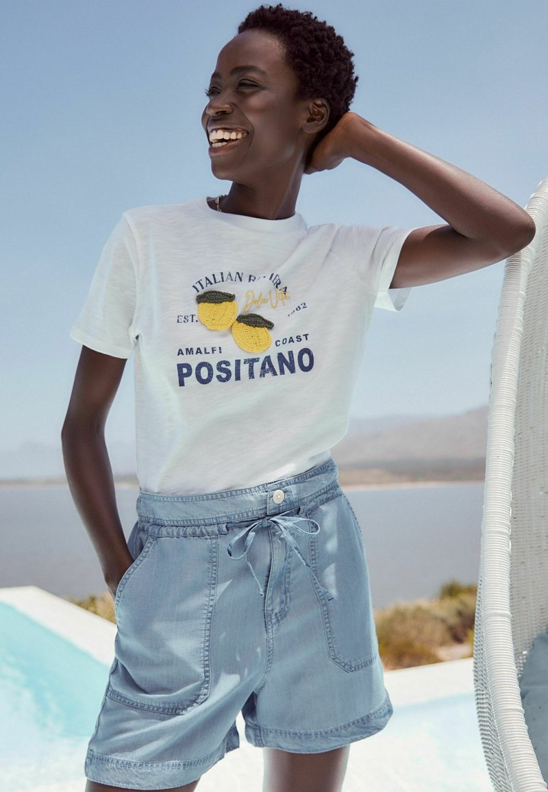 T-shirt en coton blanc avec broderie marine et accents jaunes, associé à un short en denim bleu clair avec cordon de serrage et poches latérales.
