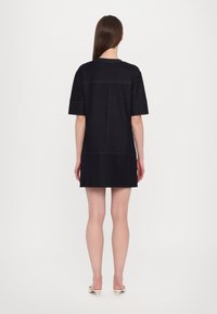 Robe en denim noir à manches courtes, coupe droite et détails de couture jaune. Possède une couture au dos et tombe au-dessus des genoux.
