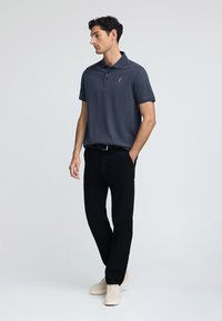 Ciemnoszary polo z kołnierzykiem, dwoma guzikami i krótkimi rękawami, w połączeniu z czarnymi spodniami i jasnobeżowymi sneakersami. Minimalistyczny design.