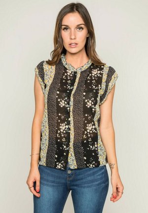 Blouse noire à manches courtes avec des motifs floraux et des accents jaunes, dotée d'un design à boutons sur le devant et d'un col en dentelle.