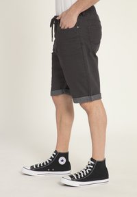 Schwarze Shorts mit umgeschlagenen Säumen, aus Denim gefertigt, mit Seiten- und Gesäßtaschen. Kombiniert mit schwarzen High-Top-Sneakern.