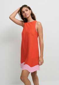 Rotes ärmelloses Kleid mit rundem Ausschnitt und einem pinkfarbenen gewellten Saum. Glatte Stoffoberfläche mit kontrastierendem Stich entlang des Ausschnitts.