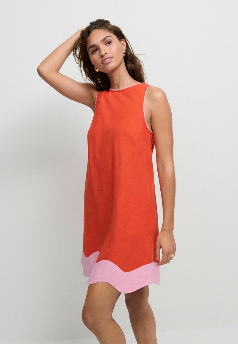 Rotes ärmelloses Kleid mit rundem Ausschnitt und einem pinkfarbenen gewellten Saum. Glatte Stoffoberfläche mit kontrastierendem Stich entlang des Ausschnitts.